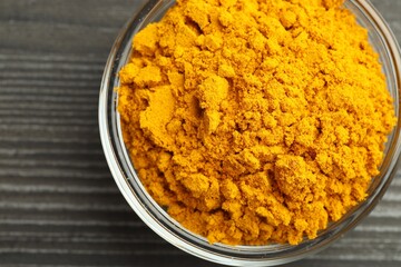 Turmeric powder in glass bowl on grey wooden table, closeup. Top view