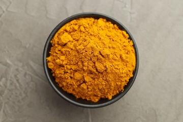 Turmeric powder in bowl on grey table, top view