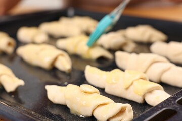Woman brushing egg wash onto raw croissants at table indoors, closeup