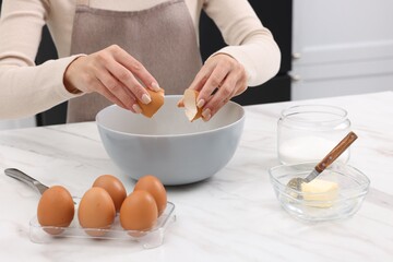 Making dough. Woman adding egg into bowl at white marble table, closeup