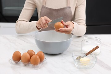 Making dough. Woman adding egg into bowl at white marble table, closeup