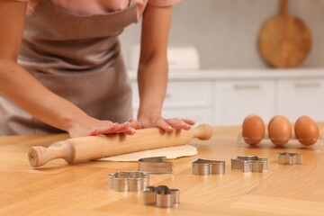 Woman rolling dough for cookies at wooden table indoors, closeup