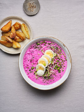 A vibrant bowl of Ukrainian borscht showcases its rich beet color, garnished with sliced eggs and herbs. Crispy roasted potatoes accompany the dish, creating a hearty meal perfect for sharing
