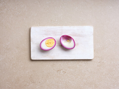 Delicious deviled eggs sit on a wooden board, showcasing their bright yellow yolks and striking purple edges. Perfect for gatherings or as a tasty snack at any time