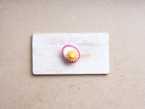 A single deviled egg sits atop a wooden cutting board, showcasing the creamy yellow filling. This cooking step emphasizes the process of creating a delicious appetizer
