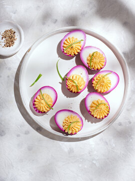 A plate features beautifully arranged deviled eggs with vibrant purple edges, showcasing a creamy filling. Ideal for parties or casual gatherings, these flavorful bites are a crowd-pleaser
