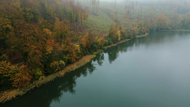 4K drone shot over scenic Kashubia. Forest and Ostrzyckie lake. Moody morning light. Fog in the background.