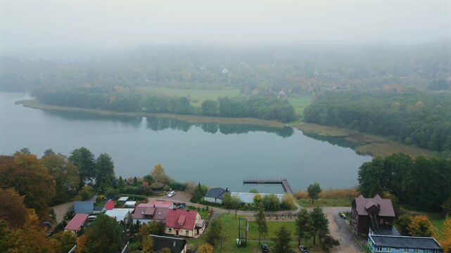 4K drone shot over scenic Kashubia. Forest and Ostrzyckie lake. Krzeszna village. Moody morning light. Fog in the background.