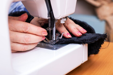 A woman skillfully uses a sewing machine to sew black fabric