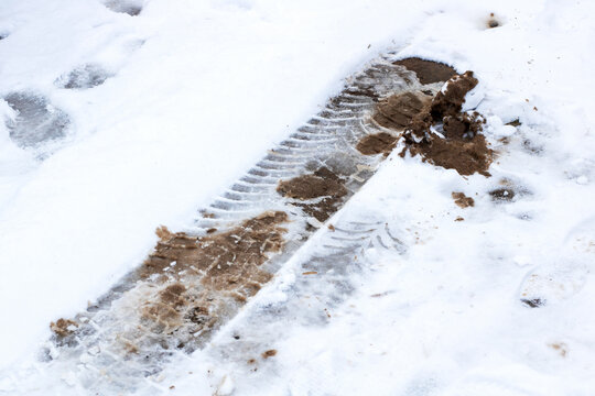 A single tire track marks the snowy landscape, covered with mud