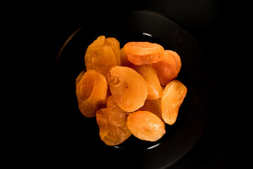 Close-up view of dried apricots arranged on a black plate highlighting their unique texture and vibrant color
