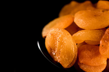 Dried apricots piled on a plate showcasing rich texture against a vivid black background