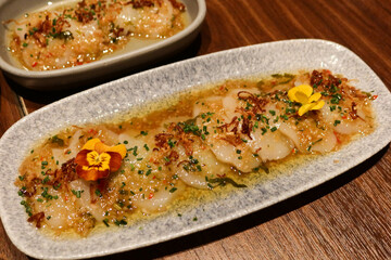 close up of Spanish tapas starter appetizer raw uncooked scallop ceviche with sauce and copy space on a white plate and wooden table