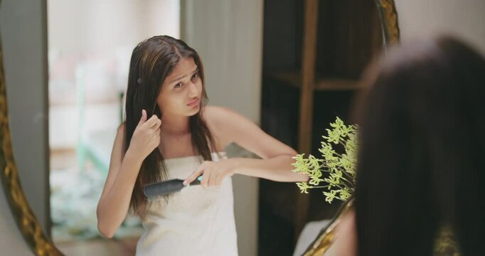 Indian Asian young adult gen z teen girl woman lady female white towel on body sad angry upset look mirror hold comb do on dry frizzy messy hair loss feel bad facing health care issue get ready day
