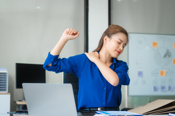 Asian businesswoman sits at her ergonomic desk, working on a laptop and mobile phone. Her posture...