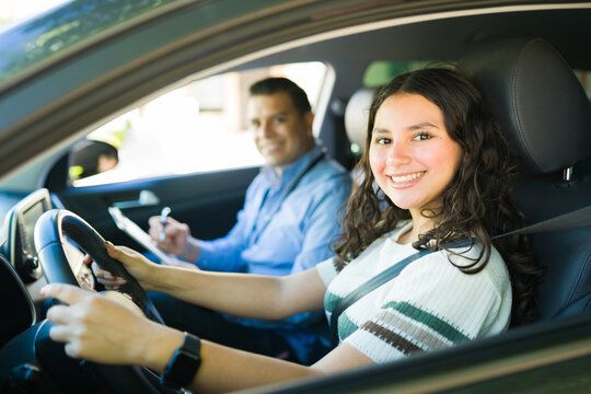 Smiling teenager learning to drive with instructor taking notes during driving lesson
