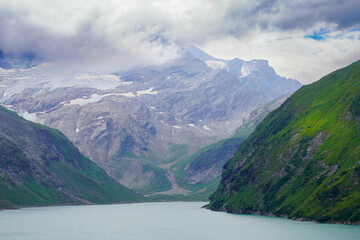 Kaprun high mountain reservoirs, Stausee Mooserboden coastline - glacier in cloudy summer day, August 20, 2024. Mountains, glacier, water reservoir  under the moody sky but nice view before the storm.