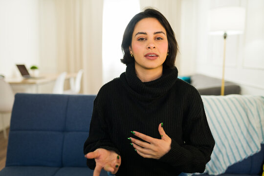 Young woman recording a vlog from her living room, talking and gesturing to the camera while streaming her video