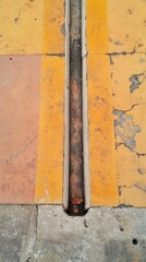 Naklejka premium A detailed view of aged pavement featuring a drainage line integrated between faded yellow stripes. The surface shows signs of wear and urban life, set in a city environment