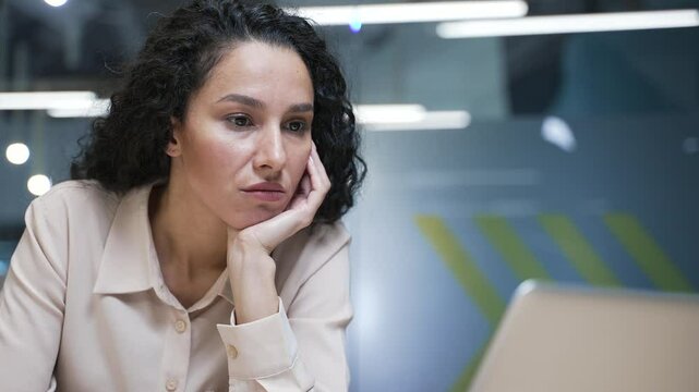Businesswoman is bored sitting at workplace at desk in modern business office. Exhausted female employee is tired from working with laptop. A lazy worker procrastinates, gets distracted. Close up