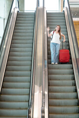 Viajera llegando y saludando desde las escaleras mecánicas de un aeropuerto © Javier
