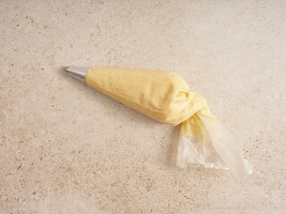 A yellow piping bag filled with frosting lays on a textured surface in a kitchen. The bag is twisted at the top, ready for decorating baked goods or pastries