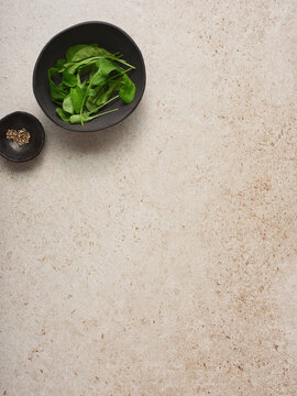 Fresh green leaves rest in a bowl alongside a small dish of spices on a light countertop. The setup highlights an emphasis on healthy cooking and natural ingredients