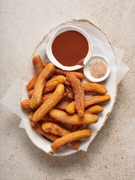Freshly made churros are plated elegantly, paired with a bowl of smooth chocolate sauce and a side of cinnamon sugar for dipping, highlighting a delightful treat