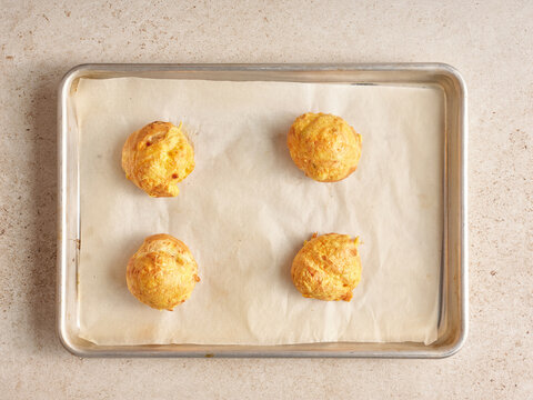 Four golden, fluffy gougeres made from choux pastry rest on a lined baking sheet, perfect for a casual gathering or an elegant appetizer, inviting everyone to savor their buttery goodness