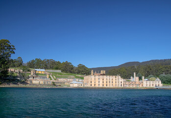 Fototapeta premium Historic ruins at Port Arthur Tasmania surrounded by lush greenery and calm waters under a clear blue sky. Australia