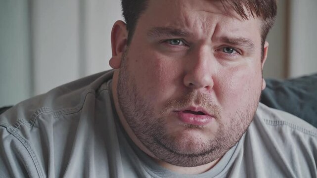 Portrait closeup of a young fat chubby man is concerned worried upset, looking at the camera.