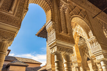 Fototapeta premium The Court of the Lions at the Alhambra complex in Granada town, Andalusia, Spain. Arabesque stonework and arches of a historic building against a bright blue sky.