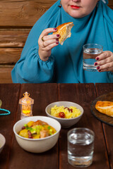 Woman in light blue hijab eating iftar bread at table during Ramadan