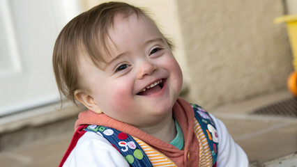 Happy baby with Down syndrome smiling while sitting on the floor