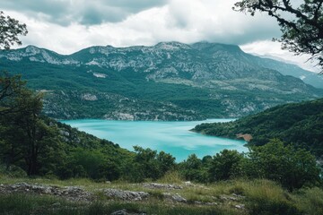Scenic view of turquoise lake surrounded by mountains under cloudy sky