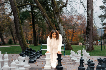 Young african female enjoying giant outdoor chess in autumn park