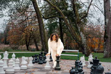 Young hispanic female enjoying outdoor chess game in autumn park