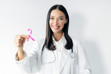 Young woman doctor holding breast cancer awareness pink ribbon over white background. World cancer...