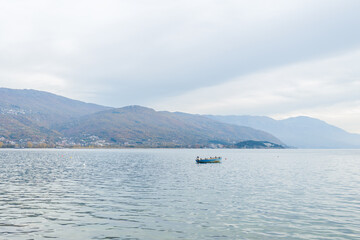 Serene, minimalist scene featuring a single blue boat floating on still water, with birds perched on it. The background is misty, with faint outlines of distant mountains.
