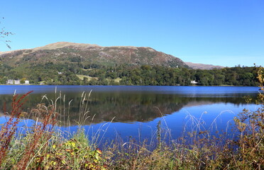Heron Pike and Lord Crag from Grasmere. Reflections in still water of lake. Clear blue sky.