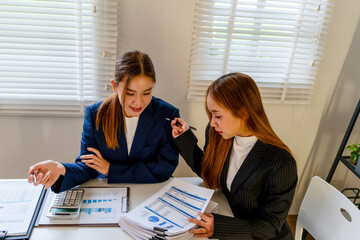 Businesswoman sitting at desk on couch in workplace or at home working on laptop and analyzing data on charts and graphs and writing on papers to make business plan and strategies for company.