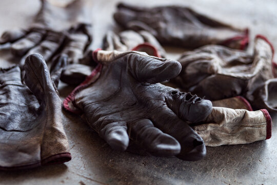 Several used dirty work gloves lying on concrete floor with blurred background.