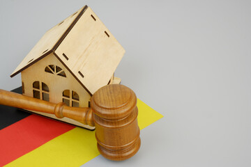 Judge gavel with wooden house model and German flag on gray background. Copy space for text.	