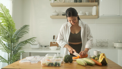 Beautiful young woman dressed in fitness wear arranging meal prep containers with healthy...