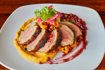 sliced duck breast on a bed of butternut squash puree with a pomegranate sauce
