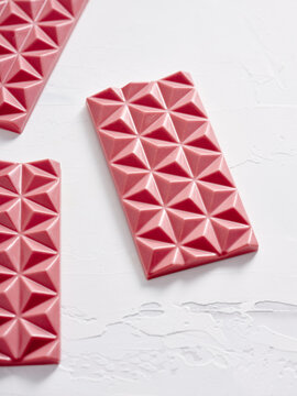 Bright pink chocolate bars with a geometric pattern are elegantly displayed on a smooth, light surface. Their vibrant color and unique shape create an appealing visual treat