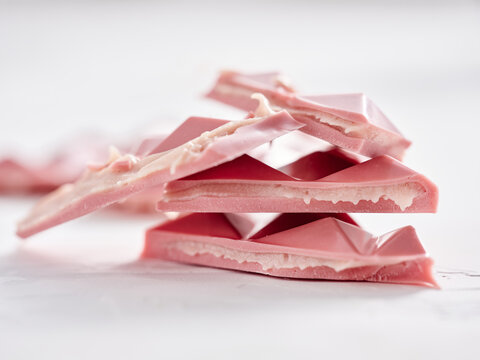 A stack of pink chocolate pieces with a creamy filling is displayed on a white surface. The geometric shapes and soft texture create an appealing and artistic presentation
