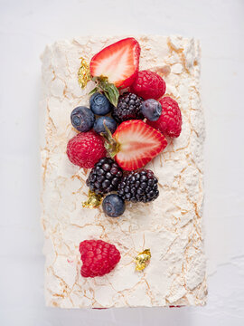 Meringue dessert displayed on a white plate, beautifully decorated with fresh strawberries, blueberries, raspberries, and blackberries, adding vibrant colors and textures