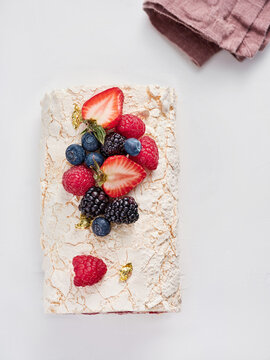 A meringue dessert is beautifully decorated with a variety of fresh berries, including strawberries, blueberries, raspberries, and blackberries, showcasing vibrant colors and textures