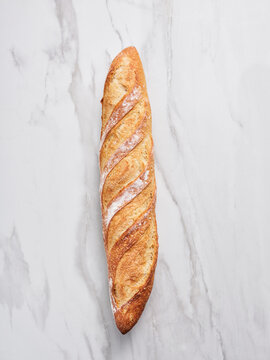 Long and golden-brown loaf of bread with a crisp crust and spiral design sits on a smooth marble surface, showcasing its artisanal appearance and inviting texture